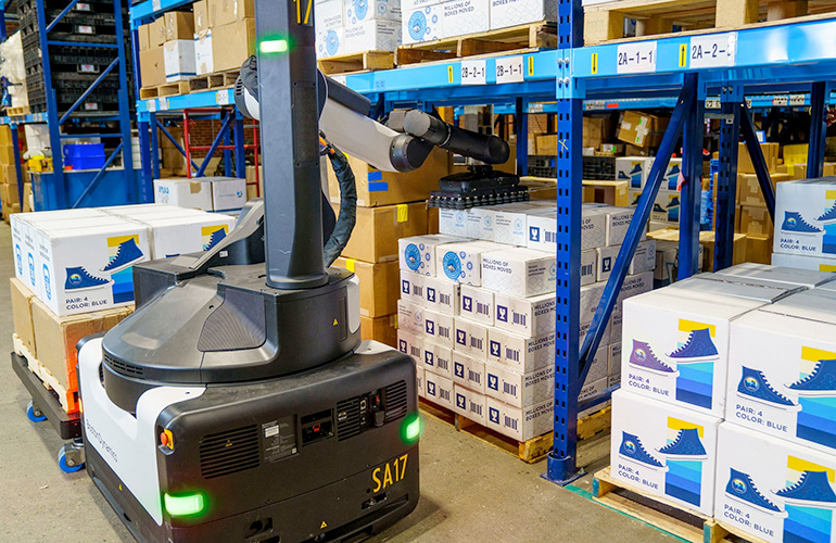 Boston Dynamics Stretch mobile robot demonstrating mobile case picking in a warehouse aisle.