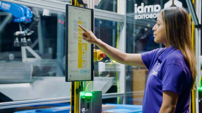 Female worker at Pitney Bowes consults a chart in front of an Ambi Robotics workcell.