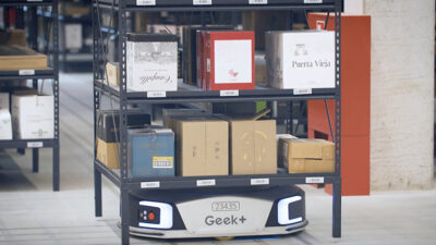 a Geek Plus AGV moves a shelf through a warehouse to a packout station.