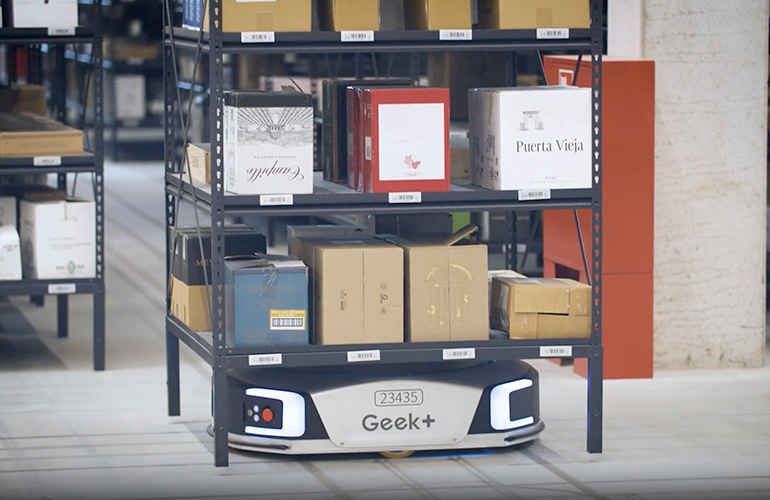 a Geek Plus AGV moves a shelf through a warehouse to a packout station.