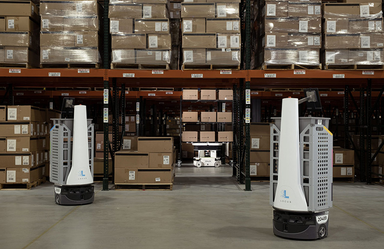 Two Locus Robotics robots in front of racks of cardboard boxes as an example of warehouse automation.
