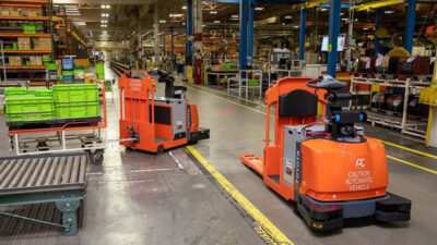 Two orange automated guided vehicles (AGVs) from Toyota Material Handling and Raymond Corp. in a warehouse.