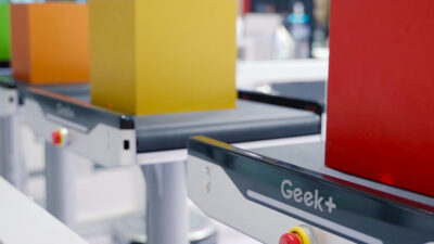 Geek+ robots with red, yellow, orange, and green boxes on top.