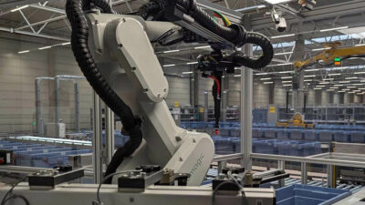 A Nomagic robotic arm picking items from bins on a conveyor belt.