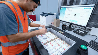 A man putting items into a box with Kardex's software pulled up on a monitor. Kardex is working with Paccurate.