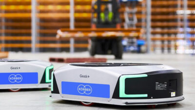 Two Geek+ mobile robots with Korber branding in a warehouse. Infios now provides warehouse software.