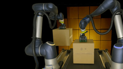 Two robot arms unloading a trailer full of boxes.