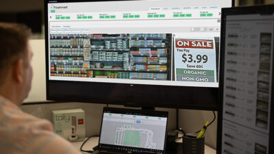 Image of a man sitting at a computer displaying a retail store planogram. Simbe for Marchants includes 'realograms' -- realtime diagrams of what's actually on store shelves.