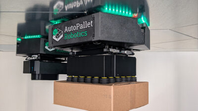The AutoPallet system uses small ceiling-mounted robots that use powerful magnets to drive upside-down on steel panels mounted overhead and reach down to pick and place cases on pallets and conveyors below.